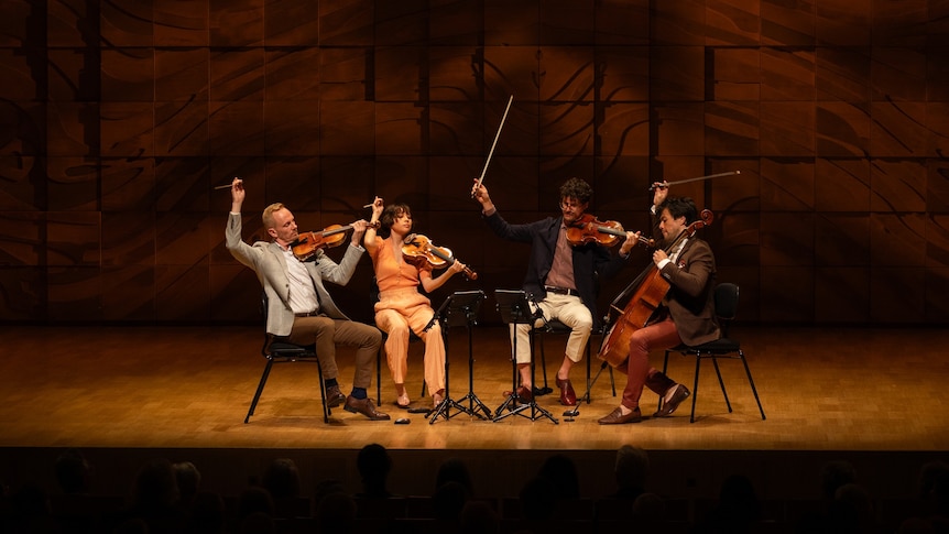 The Australian String Quartet onstage at the Elisabeth Murdoch Hall, holding their bows in the air triumphantly.