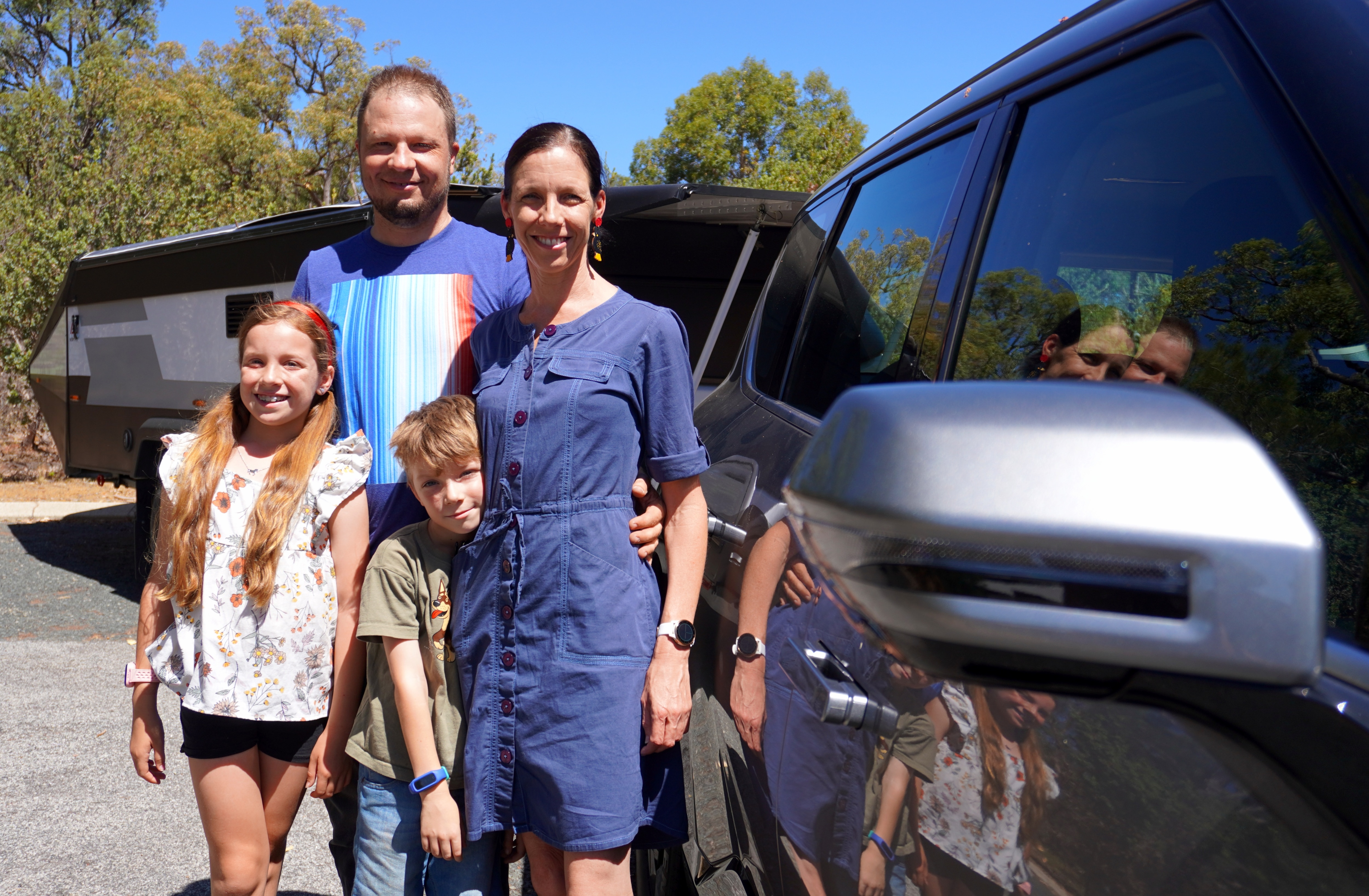 A family of four standing outside their electric 4WD and camper