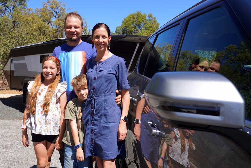 A family of four standing outside their electric 4WD and camper