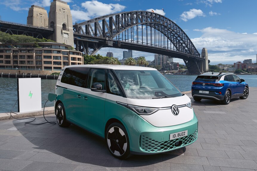 Two electric VW cars rest in front of the Sydney Harbour Bridge.