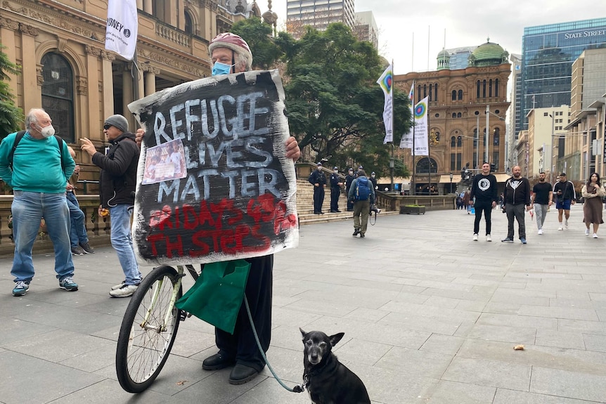 A protester and his dog hold a refugee lives matter sign