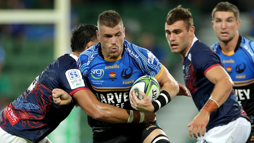 A Western Force player carries the ball while being tackled around his torso by a Melbourne Rebels opponent.