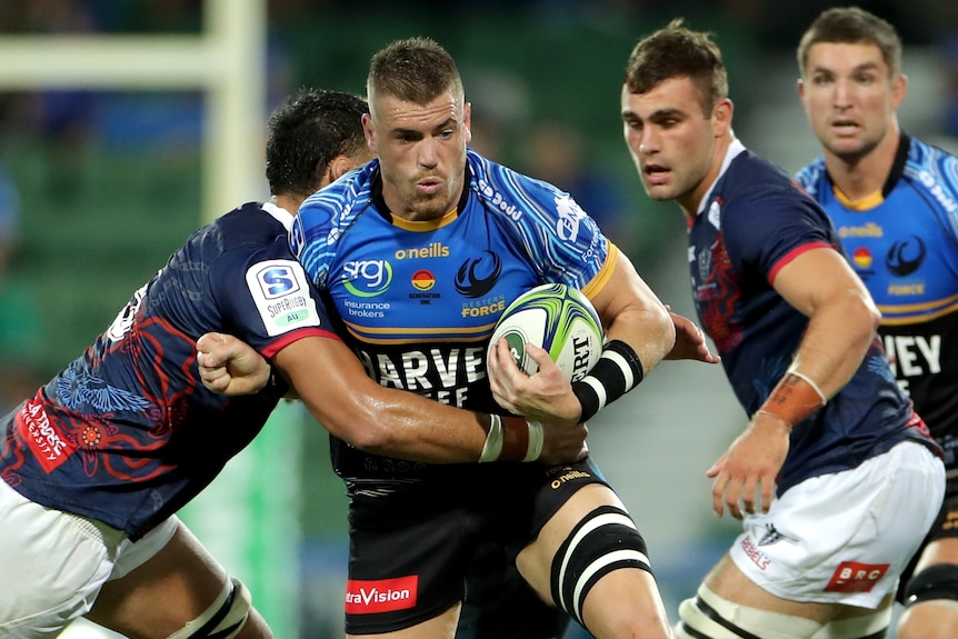 A Western Force player carries the ball while being tackled around his torso by a Melbourne Rebels opponent.