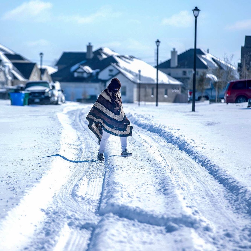 A person in a poncho and beanie walking across a snowy road