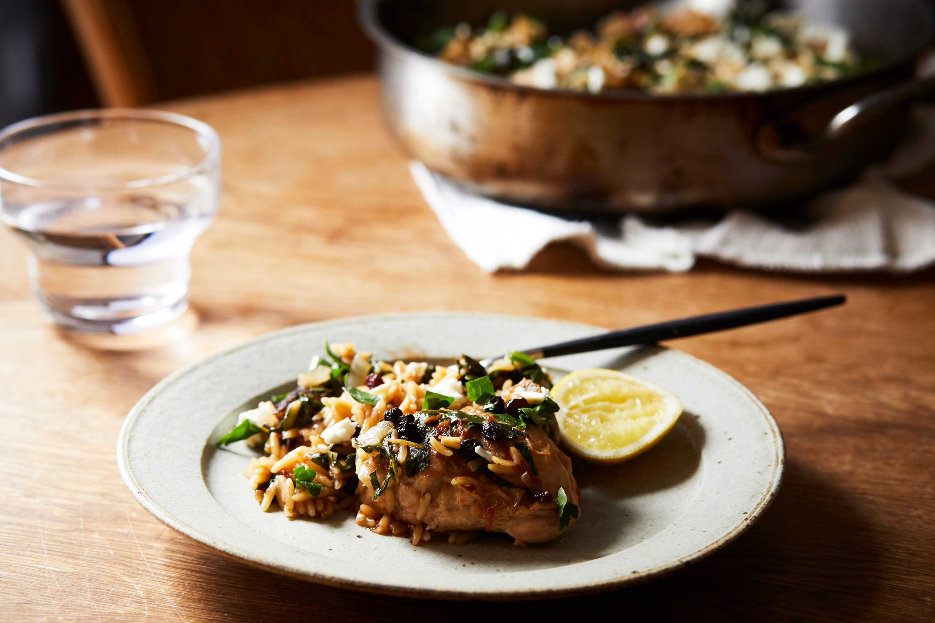 A serving of spiced chicken and risoni on a plate topped with chopped parsley, lemon and feta, a fast one pan family dinner.