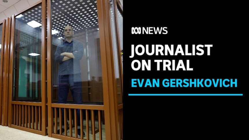 Journalist on Trial, Evan Gershkovich: A man standing in a wooden cell with perspex windows.