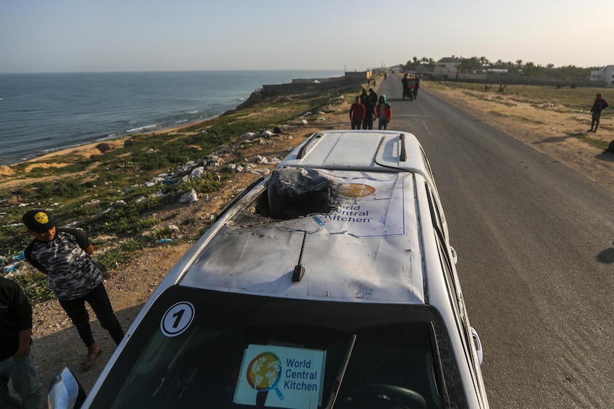 A wrecked aid vehicle on a road near the sea. 