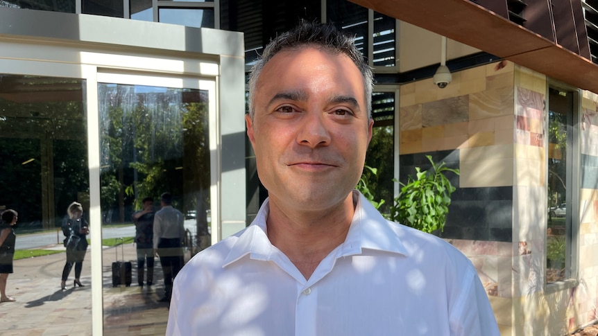 man smiles in white shirt in front of court