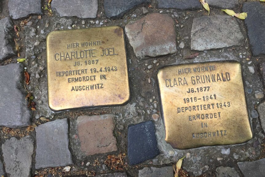 Two brass plates set in the cobblestones of a Berlin footpath. They state "Here lived" and then give the name of a person.