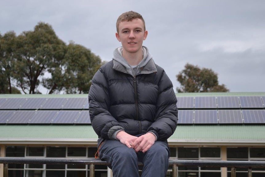 Tony Thorpe sitting in front of 125 new solar panels on the roof of the Huonville High School