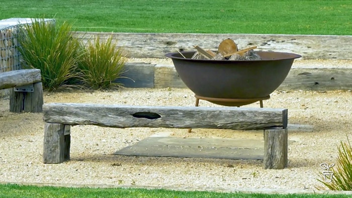 Wooden benches on gravel surface with a metal bowl fire pit in the background