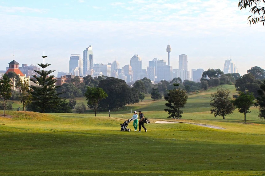 People playing golf in a large park with the city skyline in the background.