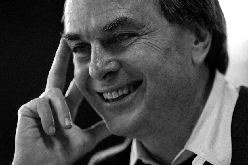 Tight black and white shot of a man smiling at something off screen.