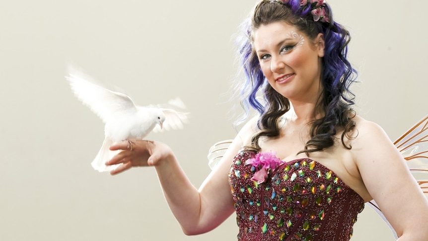 A woman in a fairy costume holds a dove on her finger.