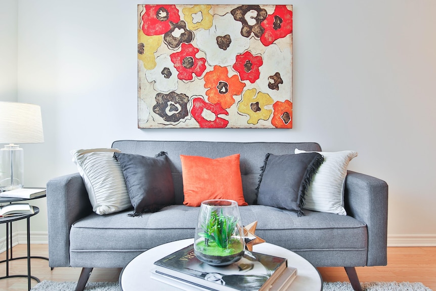 A grey couch with an abstract painting of flowers on the wall behind it.