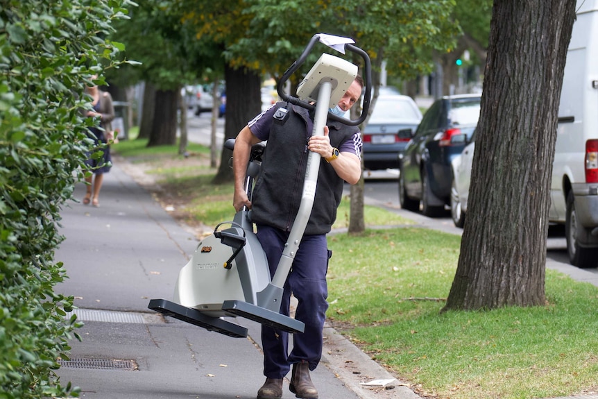 A man carries an exercise bike along a footpath.