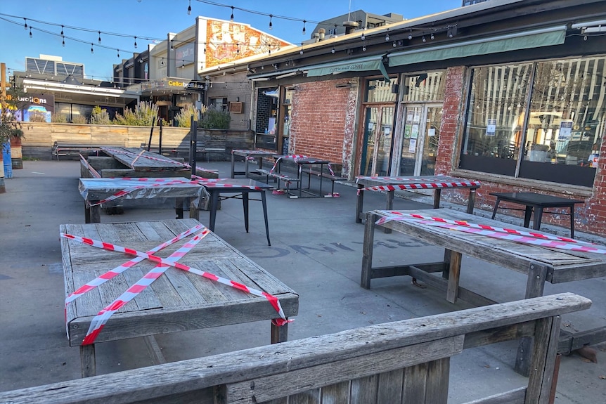 Tables have strips of tape across them to stop people from gathering in the outside area of the cafe.