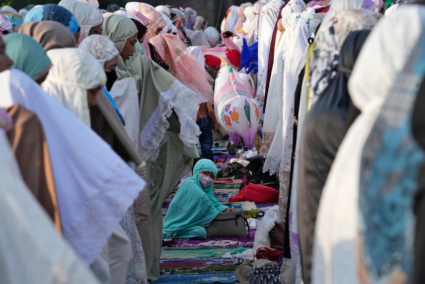 A child playing with a balloon while women in headscarves pray around her. 