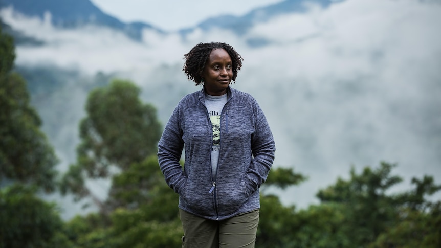 A Ugandan woman standing in front of a forest that's covered in mist.