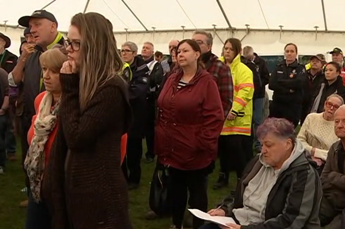 A group of people stands in a tent, many of them wearing emergency services uniforms in bright yellow and orange.