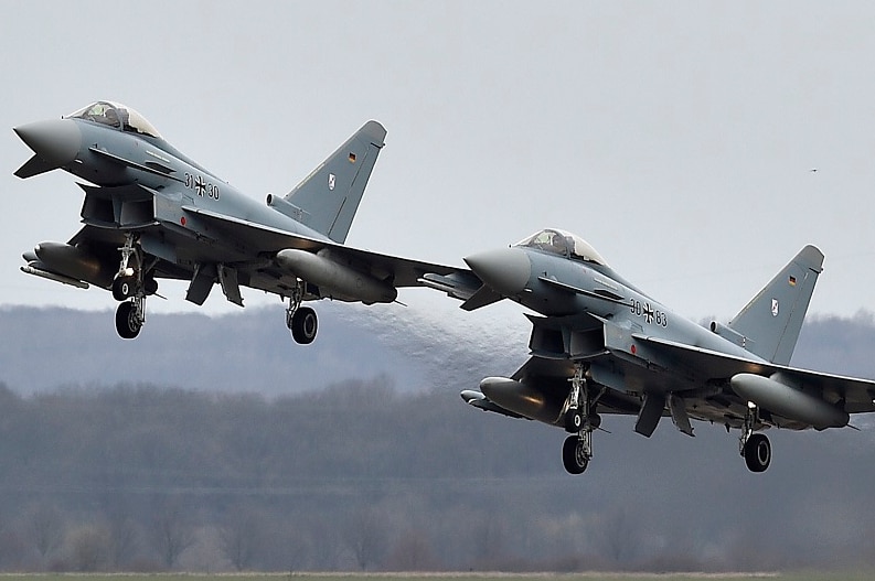 Two Eurofighter jets with their landing gear down take off in formation.