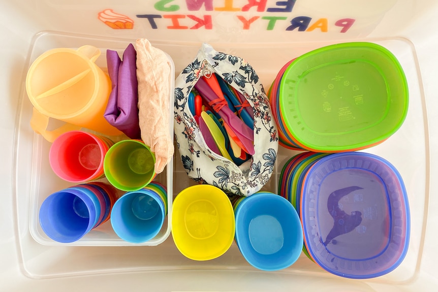 Birds-eye view into a large plastic tub kit filled with colourful plastic plates, cups and party supplies.