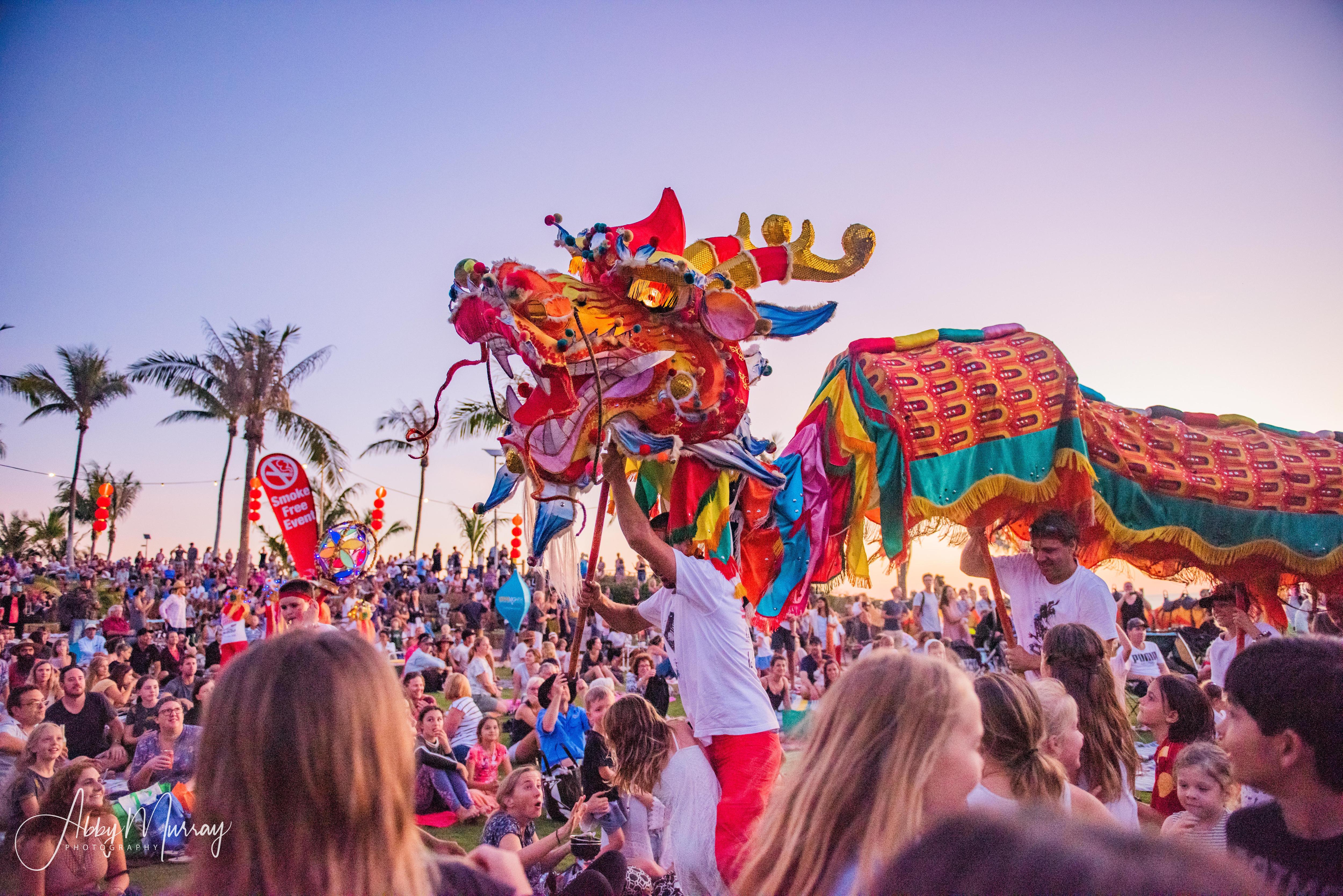 A large Chinese dragon performs for a crowd of people with palm trees in background