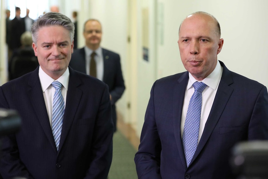 Mathias Cormann grimaces while Peter Dutton speaks beside him. Both men look disapointed.