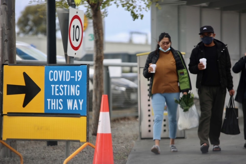 Two people walk near a sign saying 'COVID-19 testing this way'.