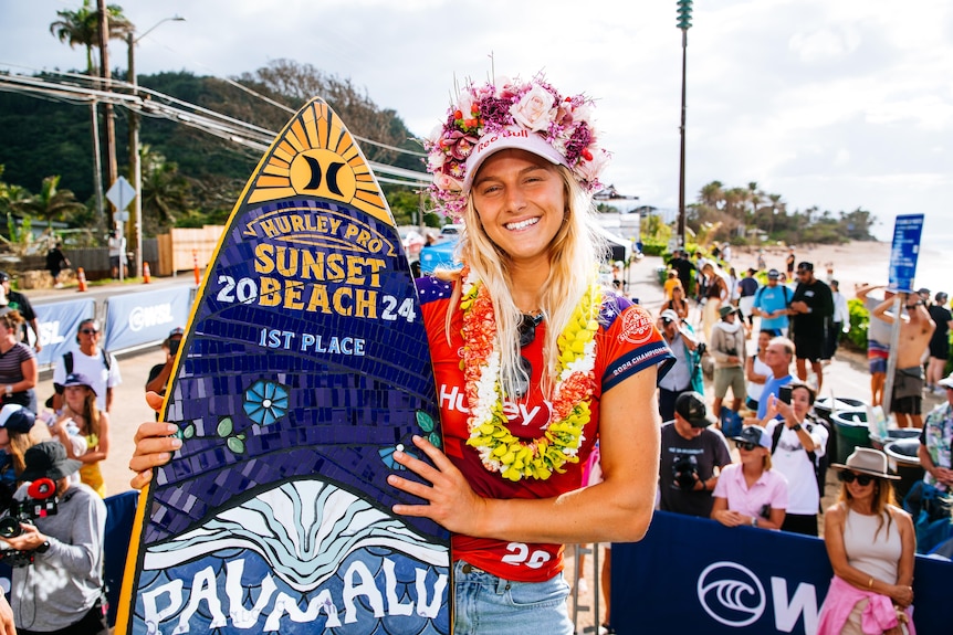 Molly Picklum smiles while holding a trophy surfboard that reads '1st place'