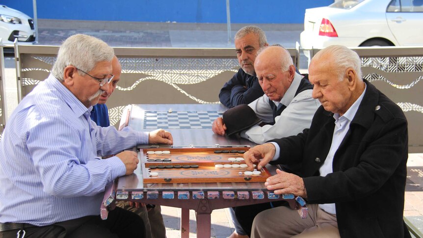Group of older men playing backgammon on picnic table.