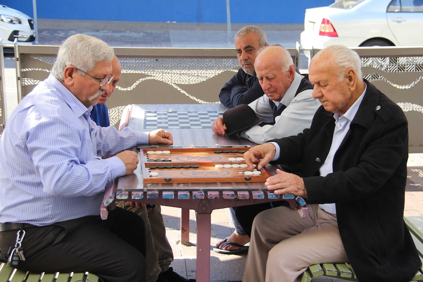 Group of older men playing backgammon on picnic table.