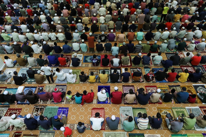 Dozens of Muslims sit on prayer mats at a mosque