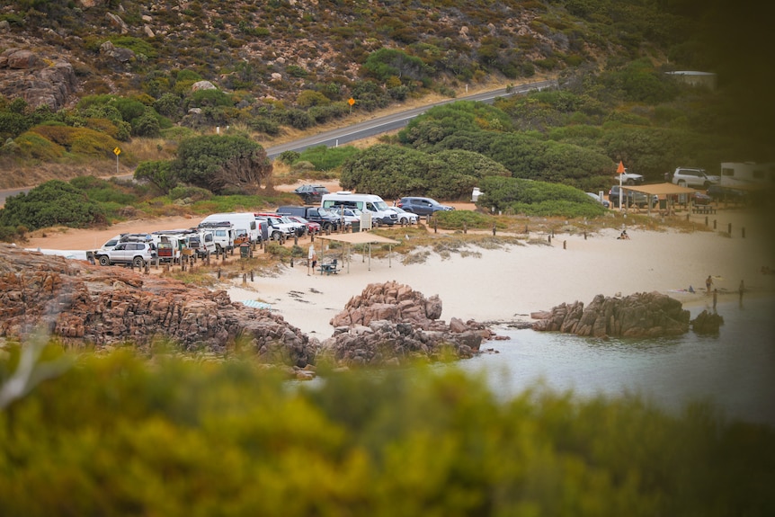 A dirt carpark filled with vans next to a beach