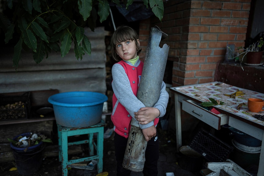 A child holds a large metal cylinder with both arms. 