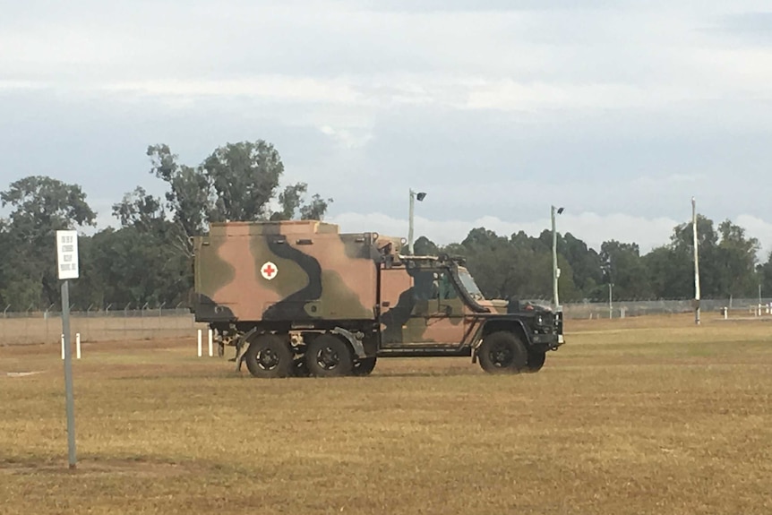 A military truck with a red cross is pictured in a brown grass field