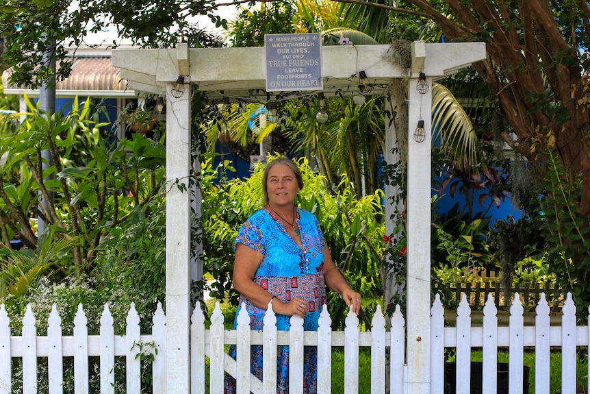 Woman standing in front of house behind a white fence.