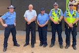 Four police offices and a man in a shirt stand in a row.