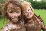 Two children covered in mud cuddling.