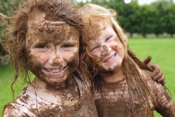 Two children covered in mud cuddling.