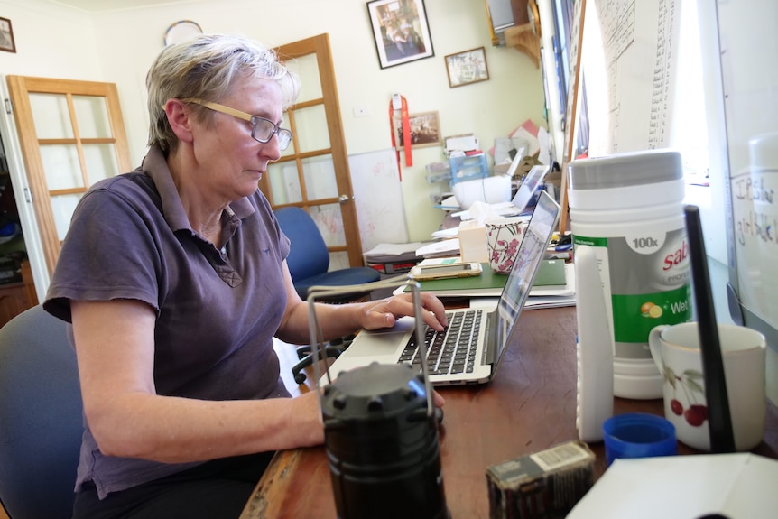 Woman in a navy blue shirt working at a laptop on a crowded desk.