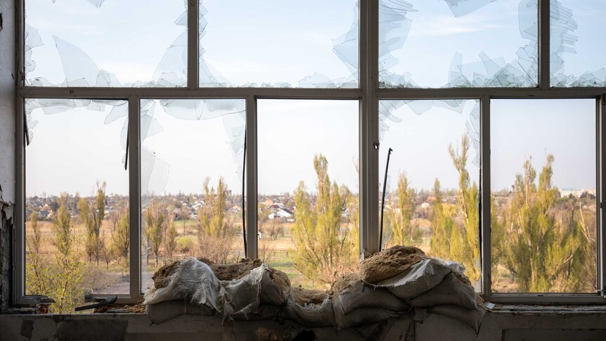 Sand bags are positioned inside a large window which has many shattered panes of glass.