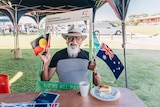 Indigenous man with hat and glasses waves Aboriginal and Australian flags 
