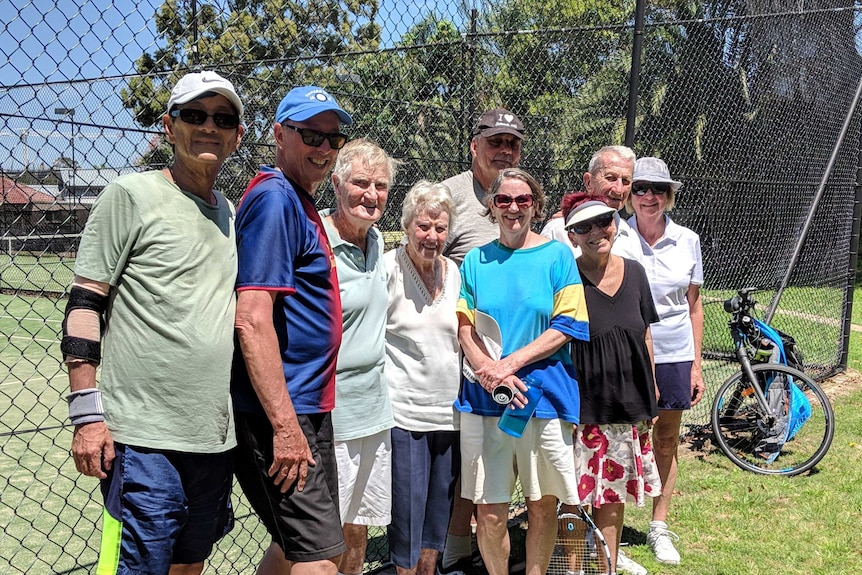 A group of people pose in front of tennis courts