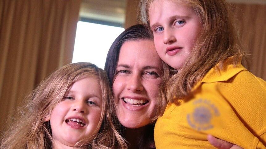 A smiling woman holding her two daughters