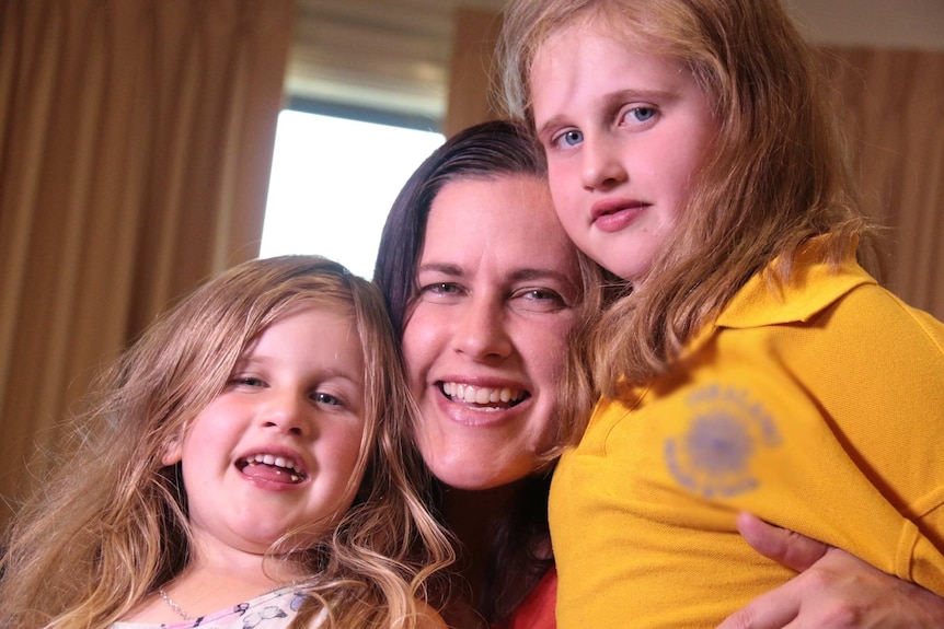 A smiling woman holding her two daughters