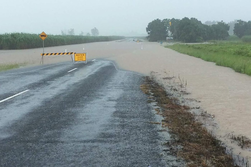 A country road under water after heavy rain, blocked by sign saying "water over road"