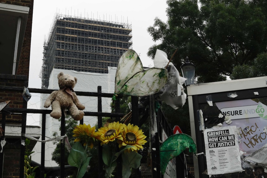 Tributes are displayed on railings backdropped by the burnt-out Grenfell Tower.