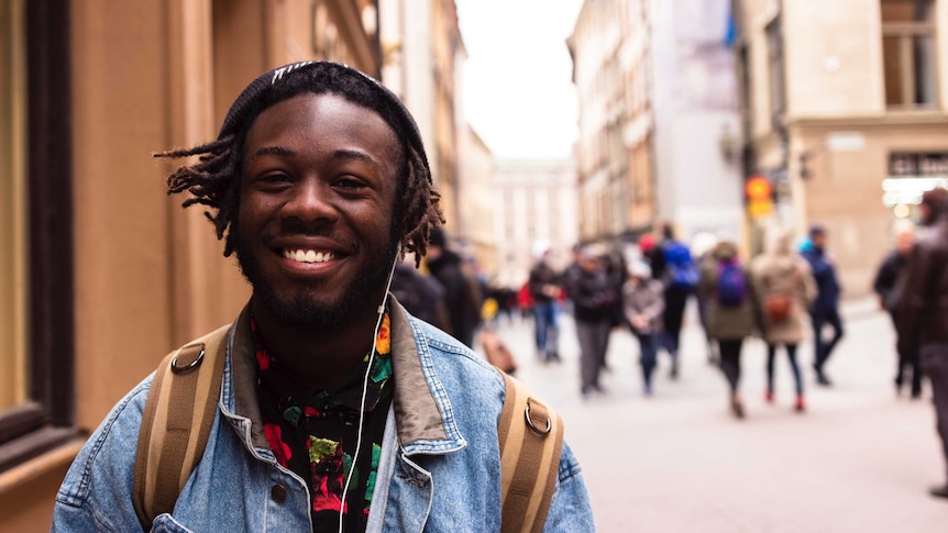 A man wearing a backpack smiles on a busy street for a story on university O-week.