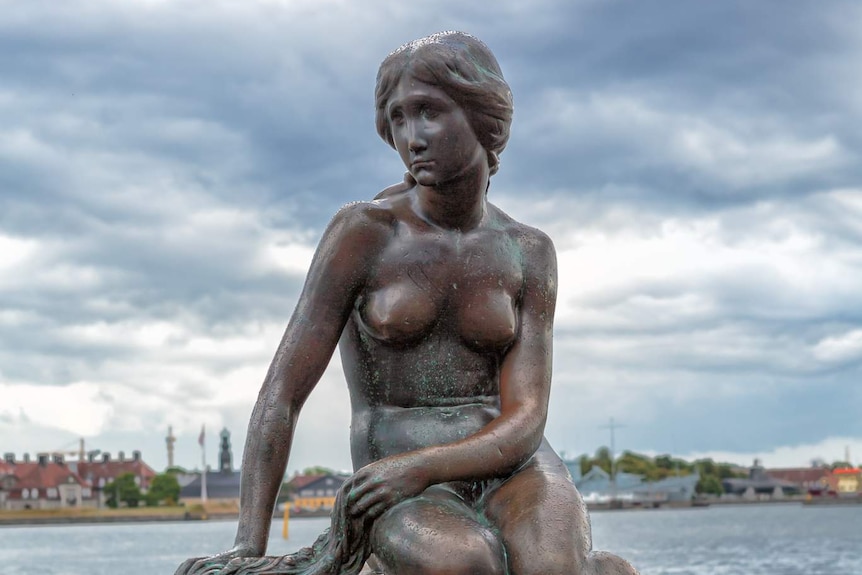 A bronze statue of a mermaid on a rock with the ocean behind